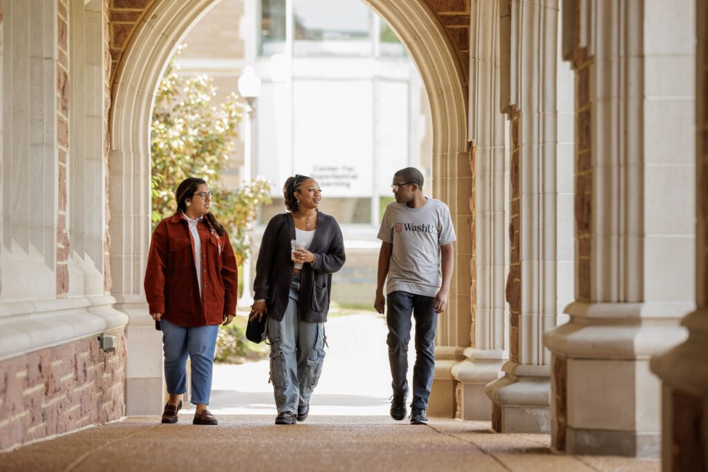 Three students walk under an archway on campus